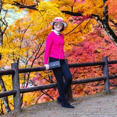 A stylish mature woman poses in front of vibrant autumn maple trees in Korankei Park, Aichi, Japan. | โครันเค (Korankei / 香嵐渓)