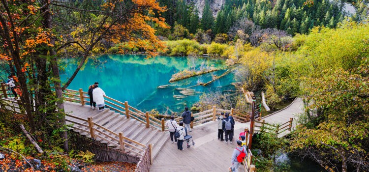 Tourists visit Jiuzhaigou Valley National Park, Sichuan, China, on October 21, 2023, enjoying autumn foliage and clear turquoise lakes along wooden walkways.